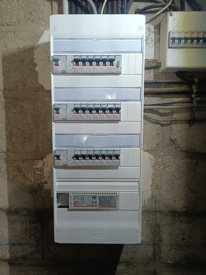 Tableau électrique à plusieurs rangées, capots blancs posés, sur un mur en parpaings